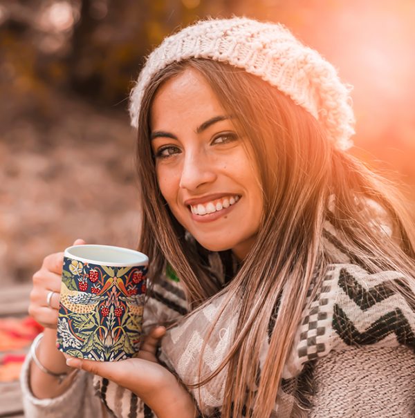 Woman holding Strawberry Thief mug outdoors drinking.